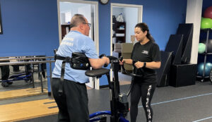 A Push to Walk trainer works with a client using equipment to walk across the gym floor