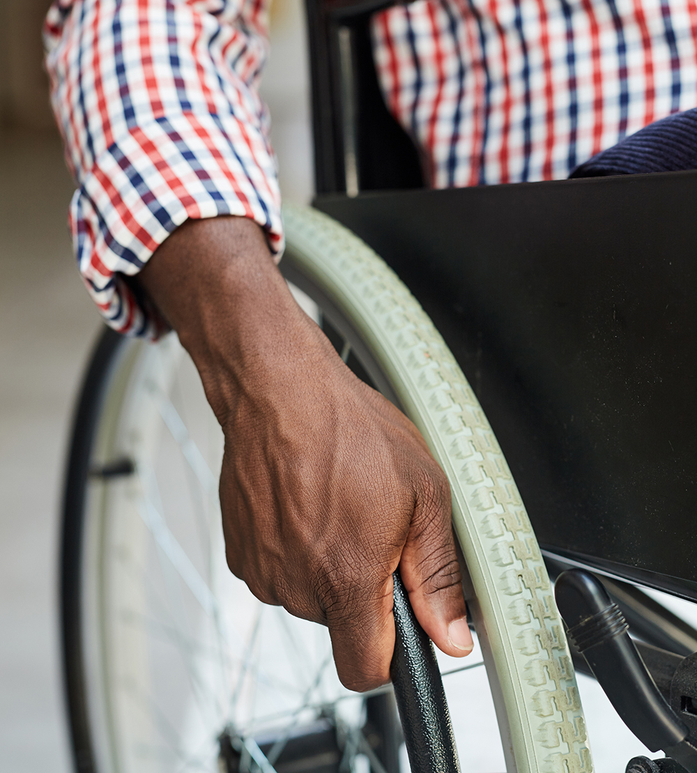 A man's hand is seen on the wheel of a wheelchair